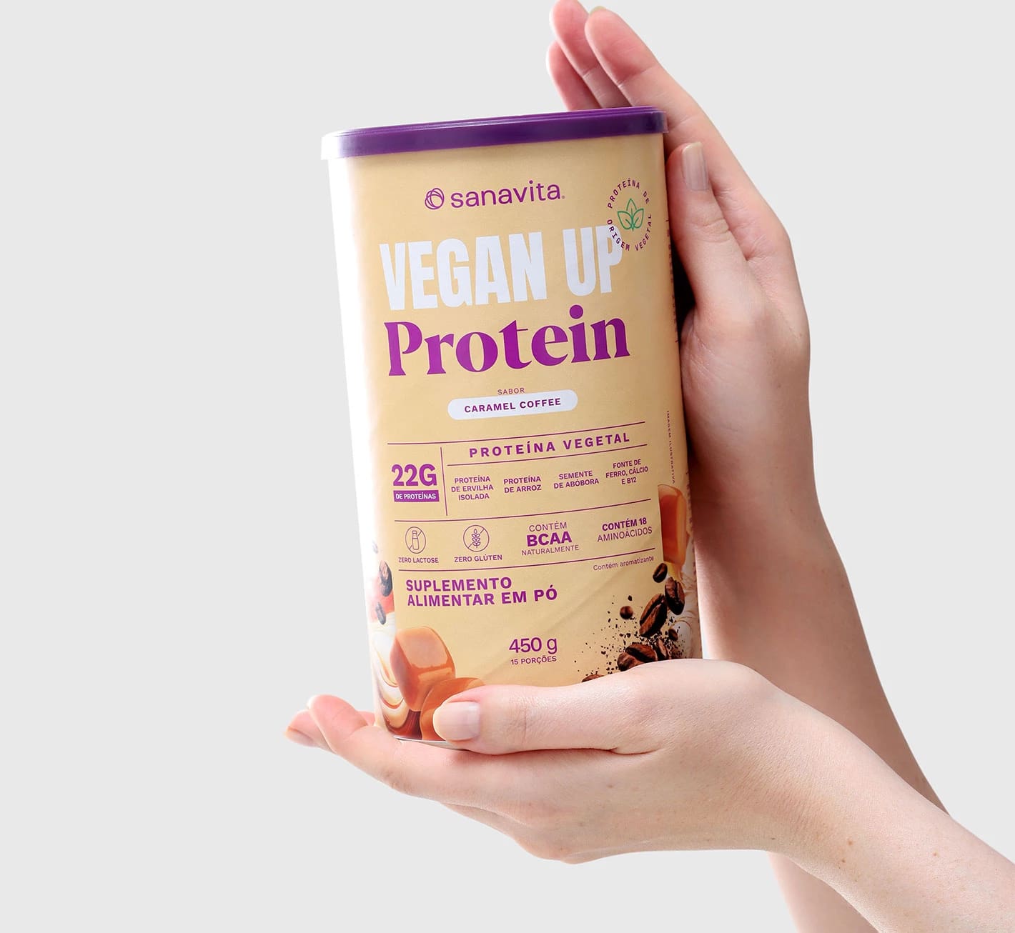 Mãos segurando um pote de proteína vegetal Vegan Up Protein da Sanavita, sabor Caramel Coffee, com informações sobre o produto, como 22g de proteína por porção e 450g no total.