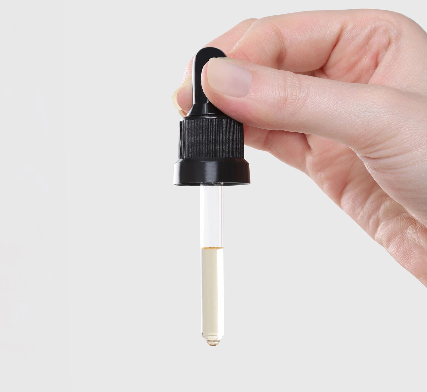 Mão segurando conta-gotas com líquido transparente parcialmente preenchendo o frasco.