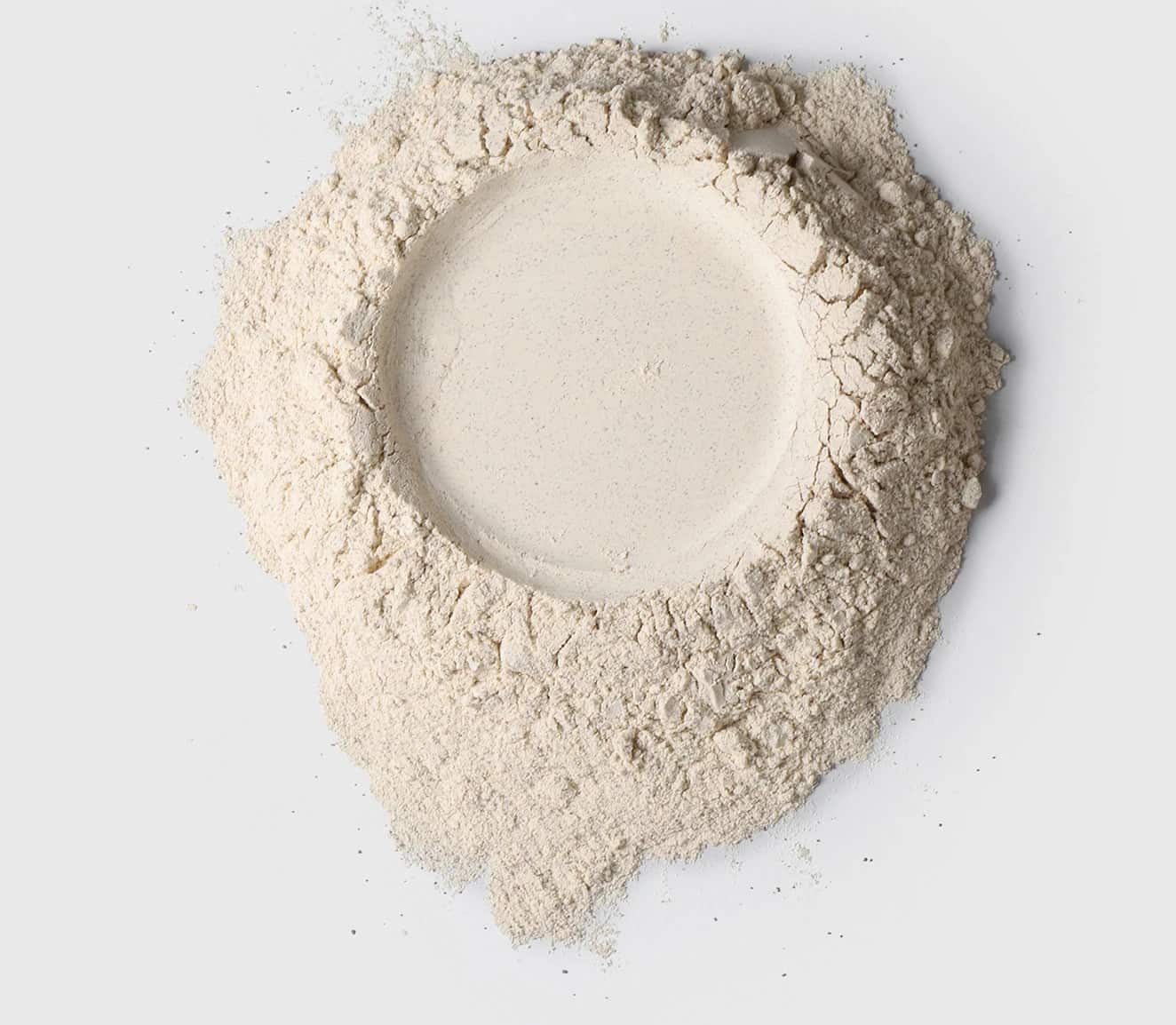 Pó branco de proteína vegetal da marca Sanavita, espalhado em forma circular com uma leve cavidade no centro.