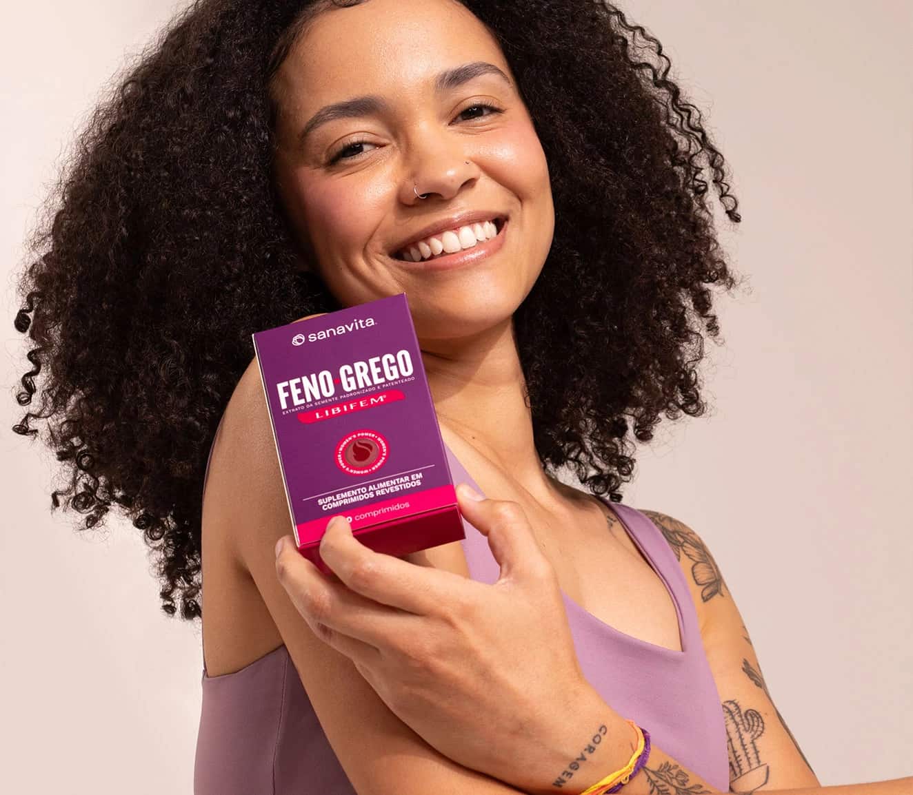 Mulher sorrindo e segurando uma caixa de suplemento alimentar Feno Grego Libifem da marca Sanavita, com destaque para o nome do produto e embalagem roxa.